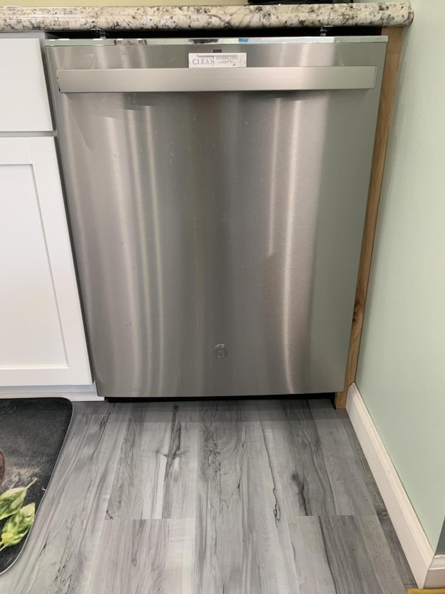 4969 N Highbridge Rd, Brethren, MI 49619 - kitchen view of dishwasher, white cabinetry, light wood-type flooring, and light stone countertops