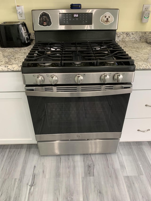 4969 N Highbridge Rd, Brethren, MI 49619 - kitchen view of stainless steel range with gas stovetop, white cabinets, light stone countertops, and wood finished floors