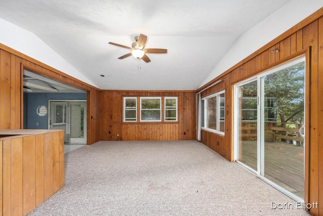 7985 Island View Dr, Newaygo, MI 49337 - unfurnished living room featuring vaulted ceiling, light carpet, a ceiling fan, and wooden walls