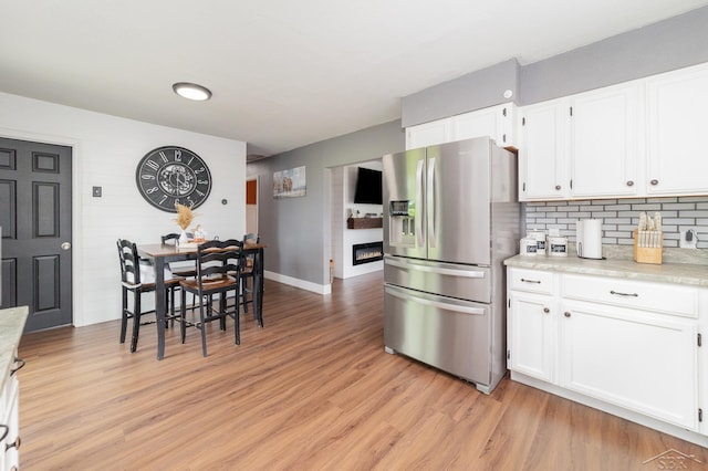 14079 Elms Rd, Montrose, MI 48457 - kitchen with stainless steel refrigerator with ice dispenser, a glass covered fireplace, light countertops, light wood-style floors, and white cabinets