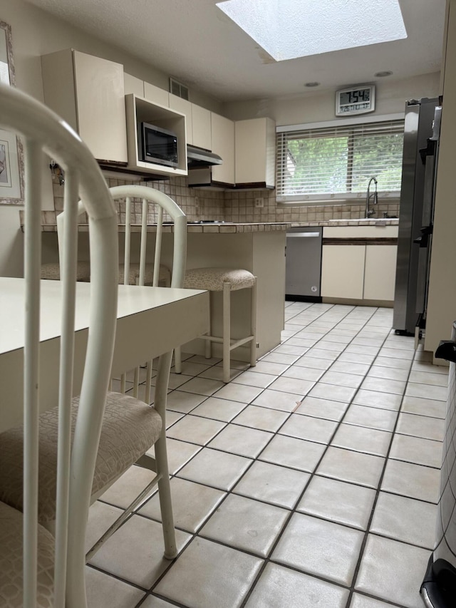 28902 Creek Bend Dr, Farmington Hills, MI 48331 - kitchen featuring a skylight, appliances with stainless steel finishes, tasteful backsplash, white cabinetry, and under cabinet range hood