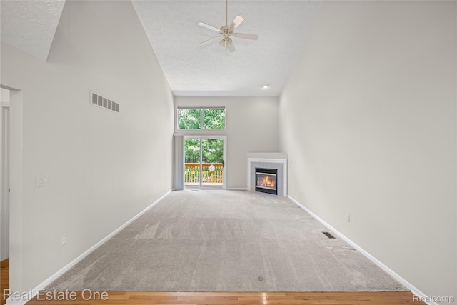 480 Hosta, Howell, MI 48843 - unfurnished living room featuring high vaulted ceiling, a fireplace with flush hearth, ceiling fan, carpet, and wood finished floors