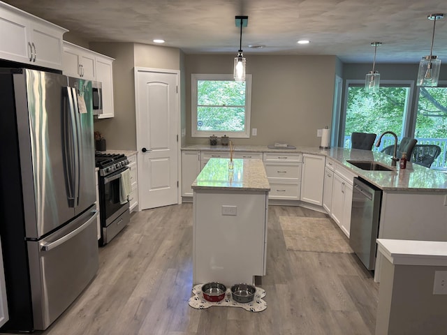 4442 Congdon Dr, Williamston, MI 48895 - kitchen featuring stainless steel appliances, a center island, light wood finished floors, white cabinetry, and hanging light fixtures