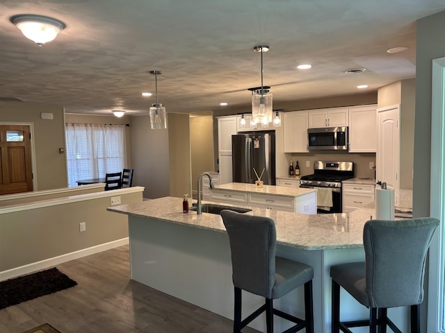 4442 Congdon Dr, Williamston, MI 48895 - kitchen with stainless steel appliances, a center island with sink, white cabinetry, dark wood-type flooring, and a breakfast bar area