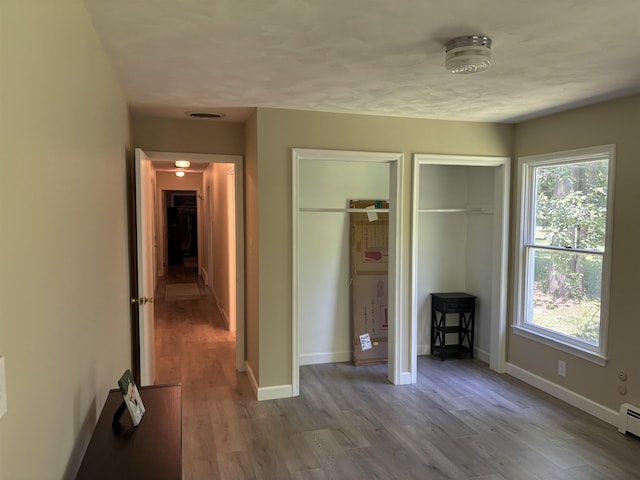 4442 Congdon Dr, Williamston, MI 48895 - unfurnished bedroom featuring two closets, a baseboard heating unit, wood finished floors, and multiple windows