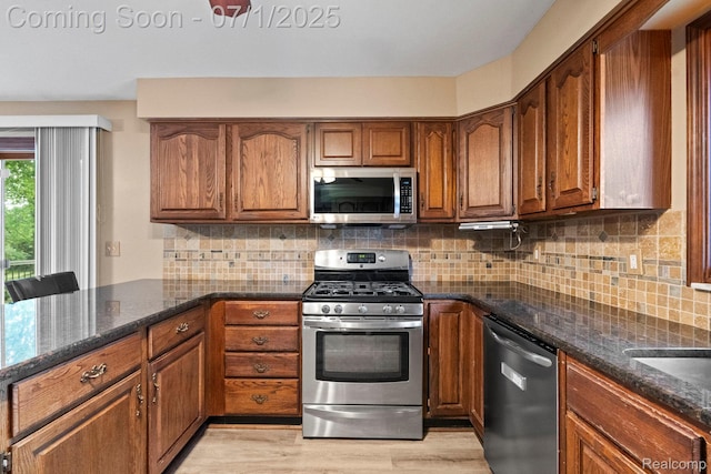 945 E Gunn Rd, Rochester, MI 48306 - kitchen featuring stainless steel appliances, brown cabinetry, dark stone counters, light wood-style floors, and decorative backsplash