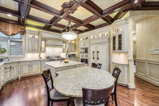 18198 Shelley Pond, Northville, MI 48168 - kitchen with appliances with stainless steel finishes, custom exhaust hood, a kitchen bar, dark wood-type flooring, and light stone counters