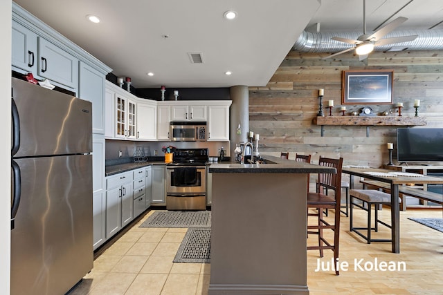 930 Washington Ave Unit 5C, Muskegon, MI 49441 - kitchen featuring stainless steel appliances, wood walls, dark countertops, a ceiling fan, and glass insert cabinets