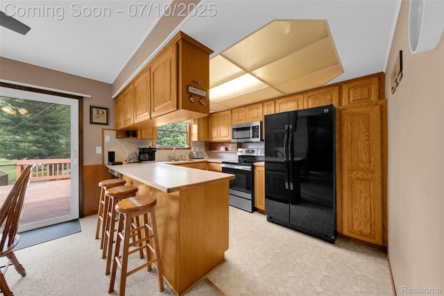2150 Dunwoodie St, Ortonville, MI 48462 - kitchen with appliances with stainless steel finishes, a peninsula, light countertops, a wainscoted wall, and a kitchen bar