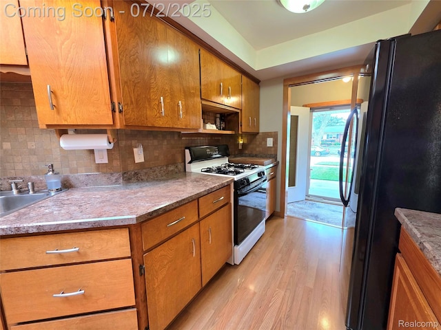 12137 Carol Ave, Warren, MI 48093 - kitchen with freestanding refrigerator, gas range, light wood-type flooring, brown cabinets, and tasteful backsplash