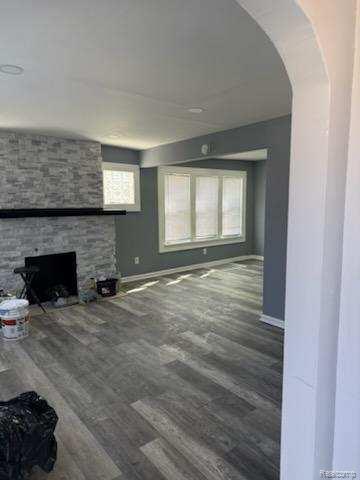 14557 Strathmoor St, Detroit, MI 48227 - unfurnished living room featuring wood finished floors, a stone fireplace, and arched walkways