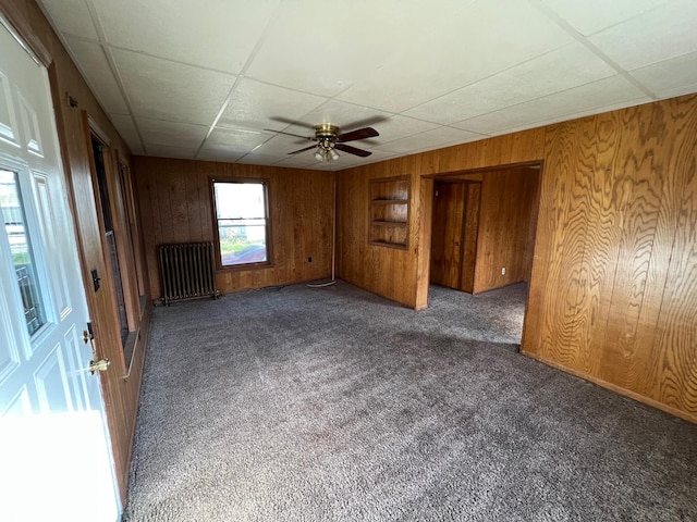 611 Steward Ave, Jackson, MI 49202 - carpeted spare room with radiator heating unit, wood walls, ceiling fan, and a paneled ceiling