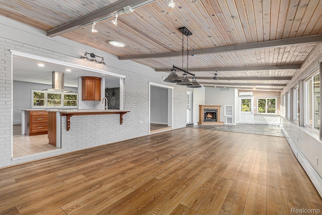 2145 Helmsford Dr, Wolverine Lake, MI 48390 - unfurnished living room featuring light wood-style flooring, track lighting, a warm lit fireplace, plenty of natural light, and brick wall