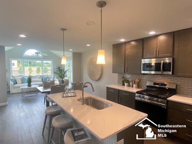 8260 Grande Lake Cir, Temperance, MI 48182 - kitchen with stainless steel appliances, tasteful backsplash, light countertops, a center island with sink, and wood finished floors