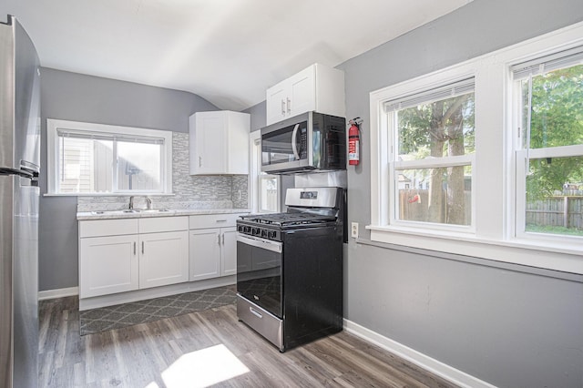 816 Oakhill St SE, Grand Rapids, MI 49507 - kitchen featuring appliances with stainless steel finishes, white cabinets, wood finished floors, healthy amount of natural light, and vaulted ceiling