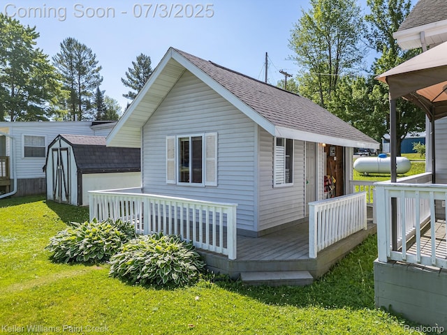 1379 Sioux St, Gladwin, MI 48624 - rear view of property with a shingled roof, a yard, a wooden deck, and a storage shed