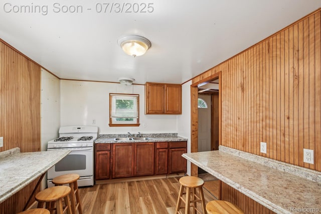 1472 Ready Ave, Burton, MI 48529 - kitchen featuring white gas stove, a breakfast bar area, light wood finished floors, wood walls, and brown cabinets