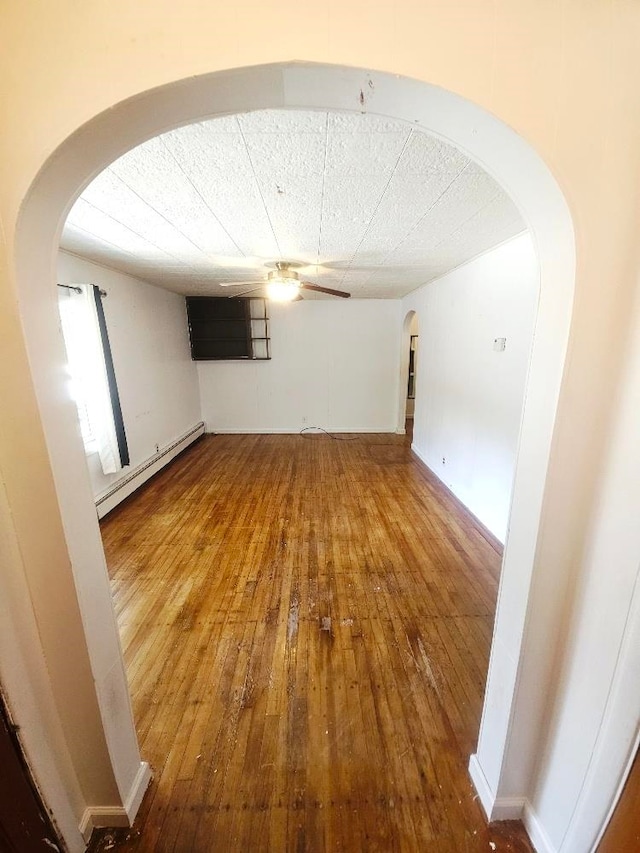 1308 W Broadway, Mount Pleasant, MI 48858 - empty room with a baseboard radiator, arched walkways, hardwood / wood-style floors, and ceiling fan