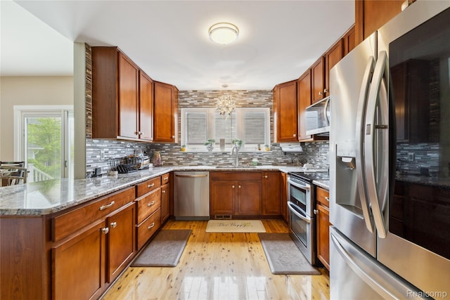 750 2nd St Unit 27, Wyandotte, MI 48192 - kitchen featuring appliances with stainless steel finishes, light wood-style flooring, backsplash, light stone countertops, and brown cabinets