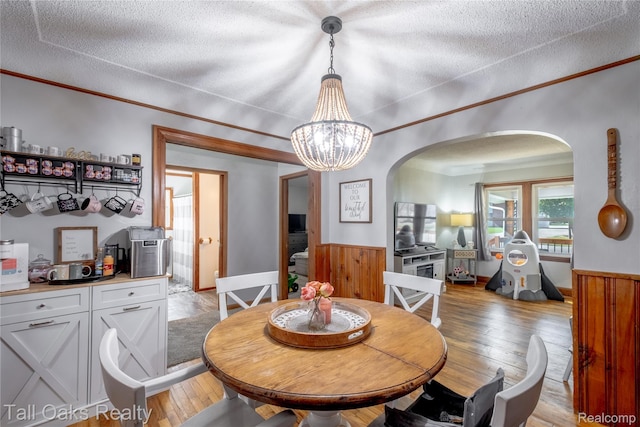 6123 Lapeer Rd, Burton, MI 48509 - dining area with arched walkways, light wood-style flooring, a wainscoted wall, a textured ceiling, and a chandelier