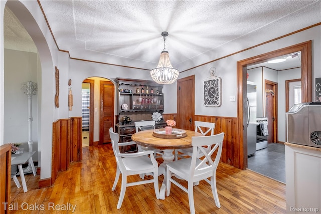 6123 Lapeer Rd, Burton, MI 48509 - dining room featuring arched walkways, wainscoting, a chandelier, light wood-style floors, and a textured ceiling