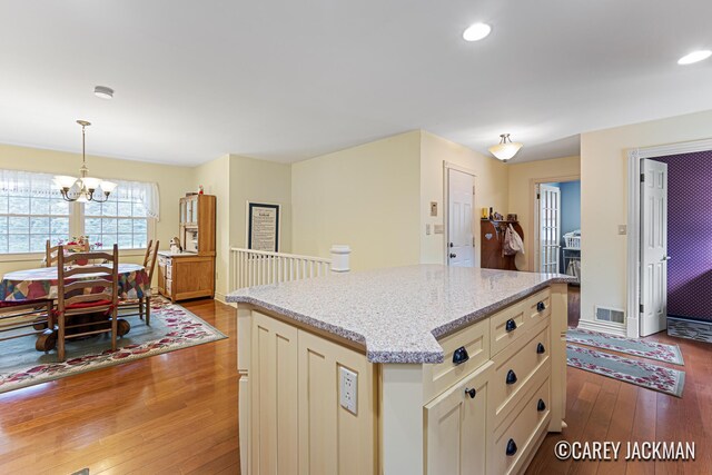 3910 Walker Ave NW, Grand Rapids, MI 49544 - kitchen with wood-type flooring, a chandelier, light stone counters, decorative light fixtures, and a center island
