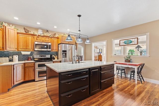 3224 Sand Creek Highway, Adrian, MI 49221 - kitchen featuring stainless steel appliances, light wood-style floors, a kitchen island with sink, hanging light fixtures, and decorative backsplash
