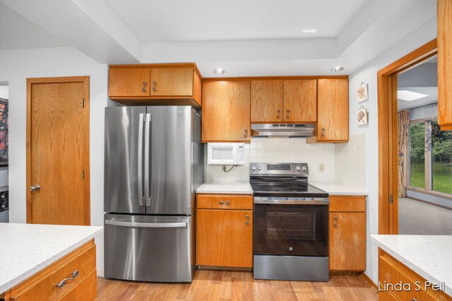6636 E Riverwoods Ct NE, Rockford, MI 49341 - kitchen with stainless steel appliances, under cabinet range hood, decorative backsplash, and brown cabinets