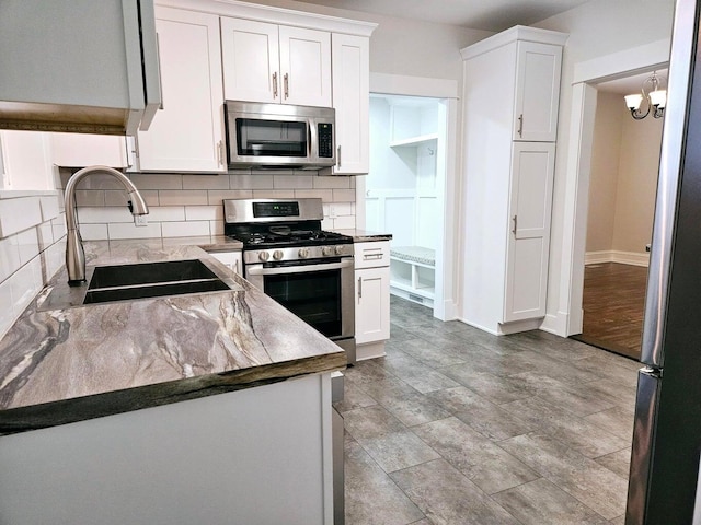 46 Lowell Ave NE, Grand Rapids, MI 49503 - kitchen with appliances with stainless steel finishes, decorative backsplash, white cabinets, and a chandelier