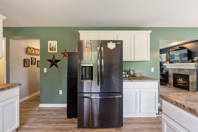 127 Ridgeview Ct, Grass Lake, MI 49240 - kitchen with stainless steel refrigerator with ice dispenser, a tiled fireplace, white cabinetry, and light wood-style floors