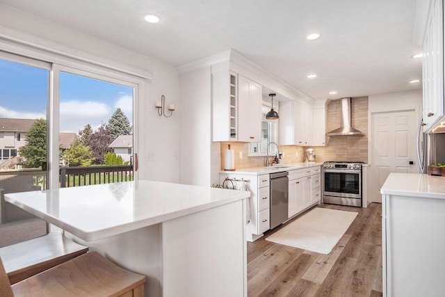 5665 Koster Dr SW, Wyoming, MI 49418 - kitchen featuring appliances with stainless steel finishes, wall chimney range hood, light wood-style flooring, white cabinets, and backsplash