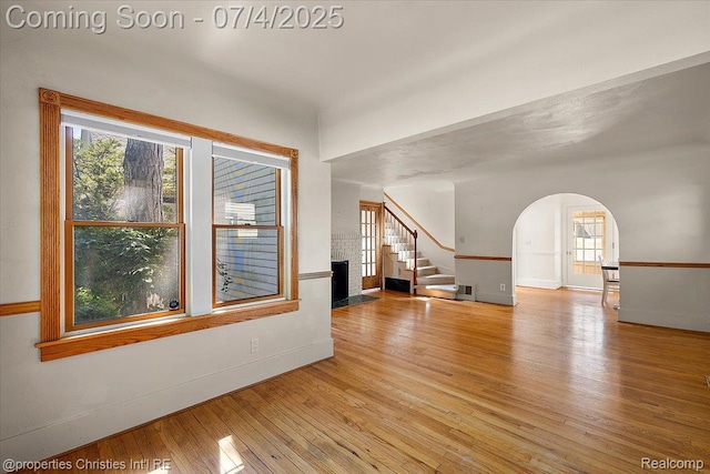 524 Oakland Ave, Birmingham, MI 48009 - unfurnished living room with light wood finished floors, arched walkways, a fireplace, and stairs