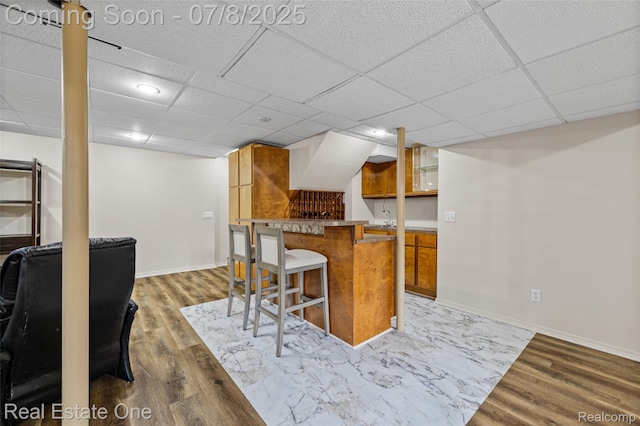17734 Huron Dr, Macomb, MI 48042 - kitchen with brown cabinetry, a kitchen bar, light wood-style flooring, a drop ceiling, and glass insert cabinets