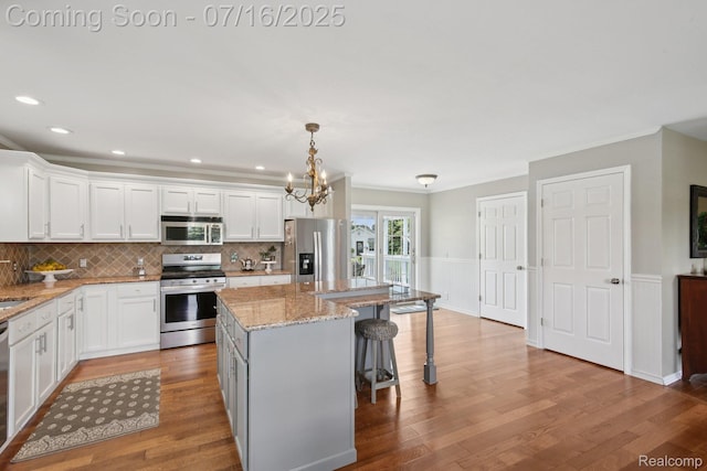 378 Fruitdale Ln, Pinckney, MI 48169 - kitchen with appliances with stainless steel finishes, white cabinetry, a kitchen breakfast bar, crown molding, and a wainscoted wall