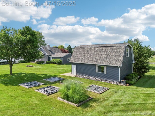 378 Fruitdale Ln, Pinckney, MI 48169 - back of house featuring roof with shingles, a gambrel roof, a yard, an outdoor structure, and a vegetable garden
