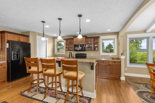 9752 Jackson Rd, Clarksville, MI 48815 - kitchen featuring black appliances, brown cabinetry, glass insert cabinets, light wood-style flooring, and a kitchen bar