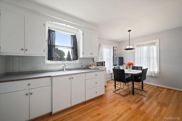 8220 Hartwell St, Detroit, MI 48228 - kitchen featuring backsplash, white cabinets, light wood-style floors, light countertops, and decorative light fixtures