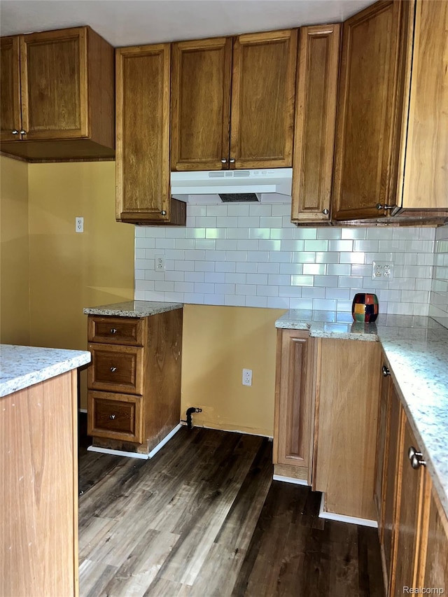 8956 Dixie Hwy, Ira, MI 48023 - kitchen with under cabinet range hood, light stone countertops, decorative backsplash, and dark wood finished floors