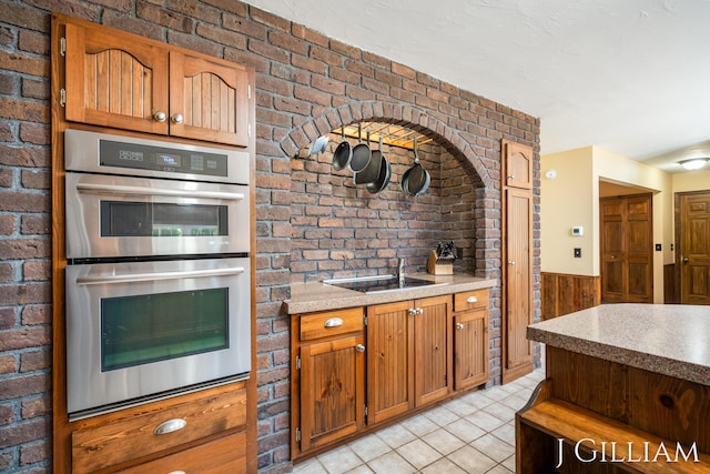 1214 Euna Vista Dr, Holland, MI 49423 - kitchen featuring stainless steel double oven, light tile patterned floors, a wainscoted wall, brick wall, and wood walls
