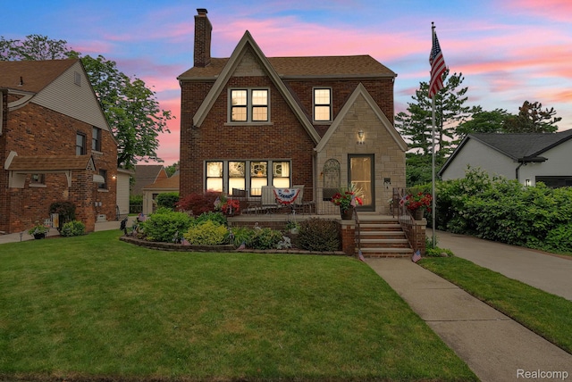 648 S Highland St, Dearborn, MI 48124 - tudor house featuring a porch, a chimney, brick siding, a yard, and roof with shingles