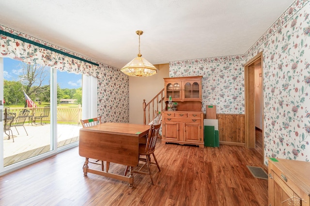 5772 Greensboro Way, Gladwin, MI 48624 - dining area with wallpapered walls, a chandelier, wood finished floors, wainscoting, and stairs