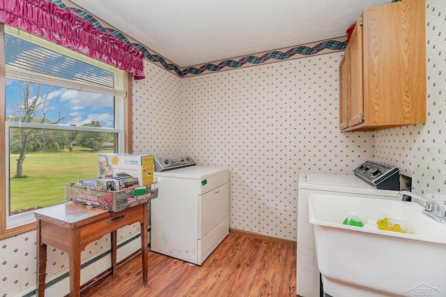 5772 Greensboro Way, Gladwin, MI 48624 - laundry area featuring separate washer and dryer, light wood-style floors, cabinet space, wallpapered walls, and a baseboard radiator