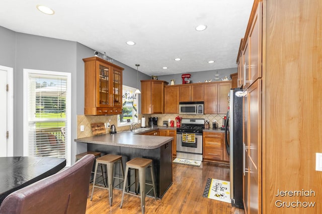 5322 S Silverstone Dr NE, Comstock Park, MI 49321 - kitchen with stainless steel appliances, a peninsula, brown cabinetry, glass insert cabinets, and recessed lighting