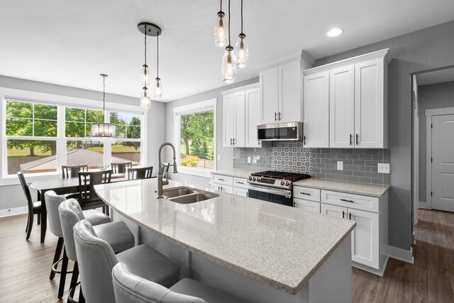 1560 Marksbury Ct, Byron Center, MI 49315 - kitchen with stainless steel appliances, backsplash, a center island with sink, wood finished floors, and white cabinets