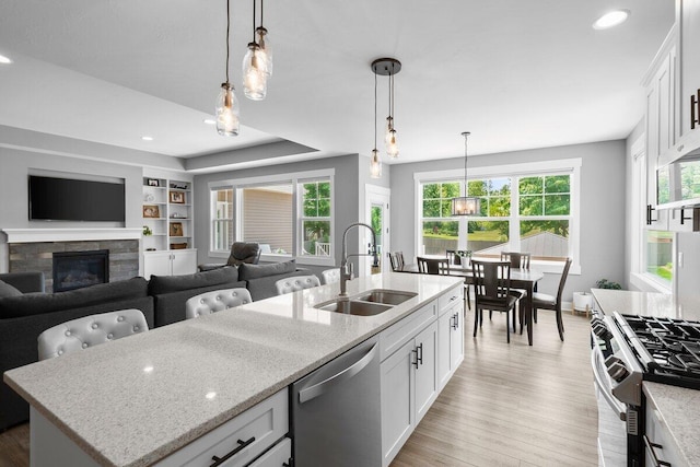 1560 Marksbury Ct, Byron Center, MI 49315 - kitchen with appliances with stainless steel finishes, a fireplace, light stone counters, light wood-type flooring, and white cabinetry