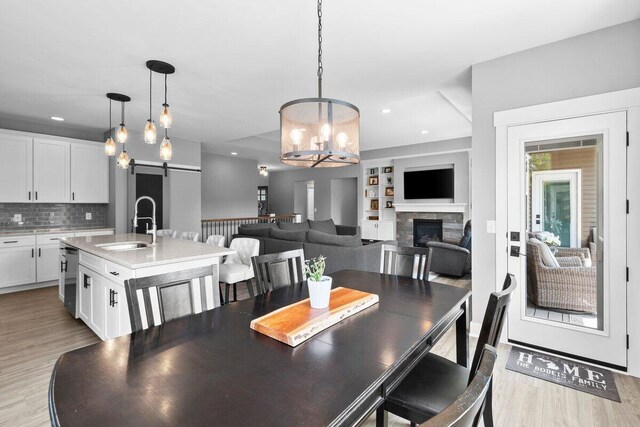 1560 Marksbury Ct, Byron Center, MI 49315 - dining room featuring a barn door, light wood-style flooring, a chandelier, a stone fireplace, and built in shelves