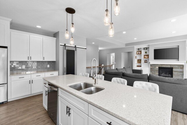 1560 Marksbury Ct, Byron Center, MI 49315 - kitchen with stainless steel appliances, a barn door, wood finished floors, hanging light fixtures, and white cabinetry
