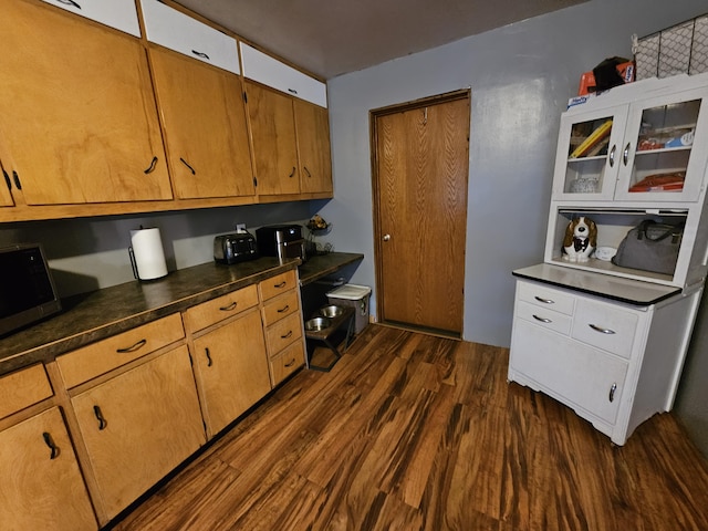 8991 W 1 Mile Rd, Hesperia, MI 49421 - kitchen with stainless steel microwave, dark wood-style flooring, dark countertops, and glass insert cabinets