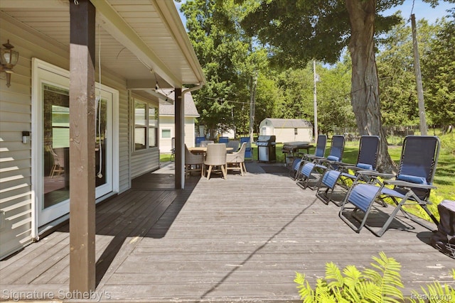 4294 N E Torch Lake Dr, Central Lake, MI 49622 - deck with outdoor dining area, a storage unit, grilling area, and view of wooded area