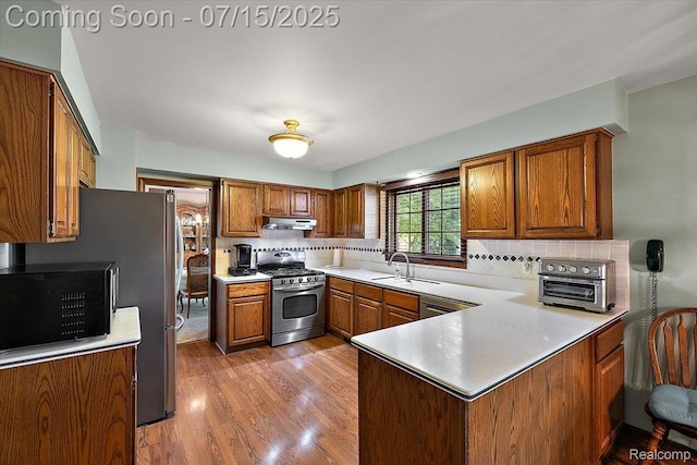 4516 Cahill Dr, Troy, MI 48098 - kitchen with appliances with stainless steel finishes, under cabinet range hood, a peninsula, brown cabinetry, and decorative backsplash